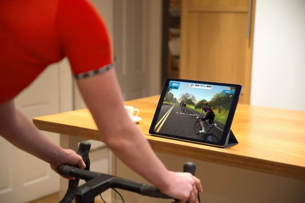 Kolesarka med zwift virtualnim treningom s tablico in cestnim kolesom.